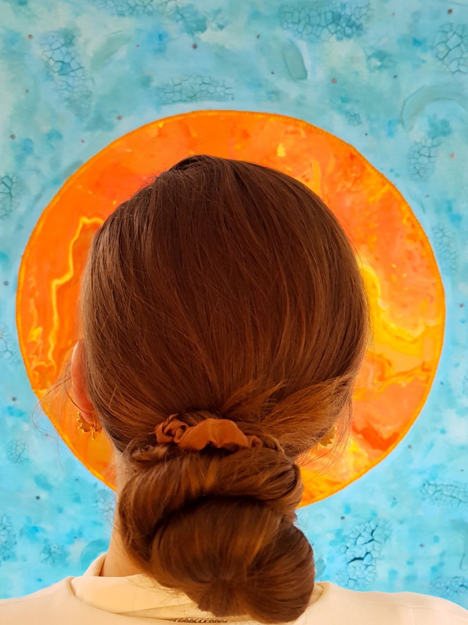 Eva Bouw voor schilderij 'the woman clothed with the sun'. Je ziet alleen de achterkant van Eva Bouw's hoofd, waarbij haar hoofd omcirkeld is dor de zon van het schilderij. 